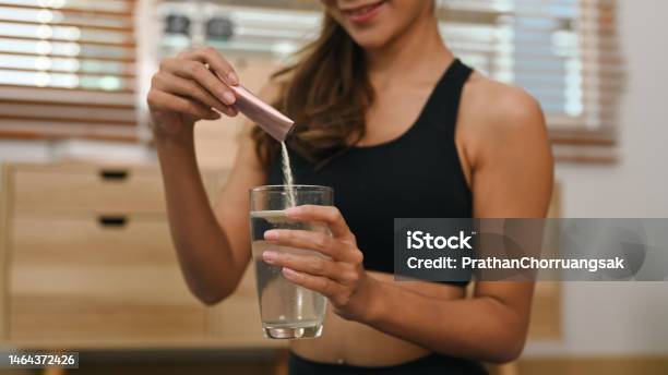 Young woman dissolving collagen powder in glass of water, preparing healthy supplement after exercise.